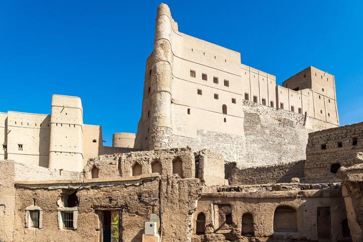 The high walls and towers of Bahla Fort above old mud-brick houses