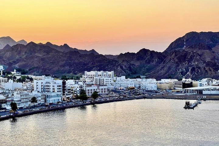 Mutrah harbour and corniche at sunset, with white buildings under the mountains