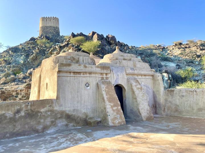 The mud and stone Al Bidya Mosque with a watchtower on the hill behind
